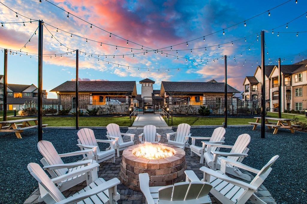 a fire pit with white rocking chairs and string lights