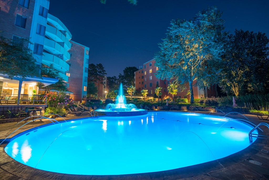 a swimming pool with a fountain in front of a building at night