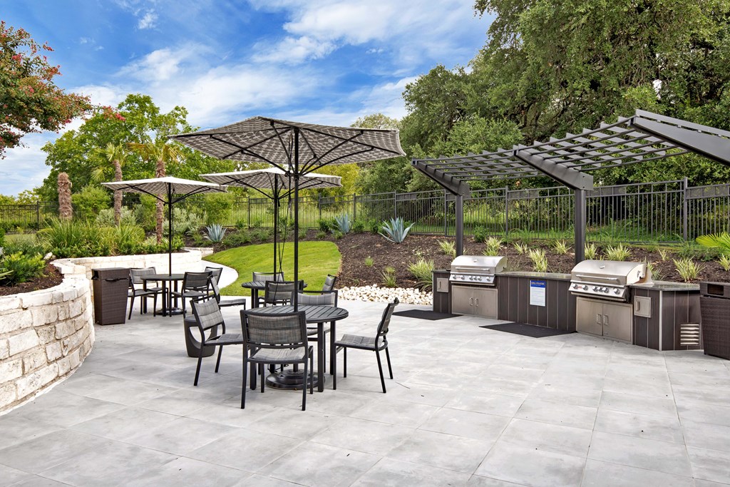 an outdoor patio with a grill and tables and umbrellas