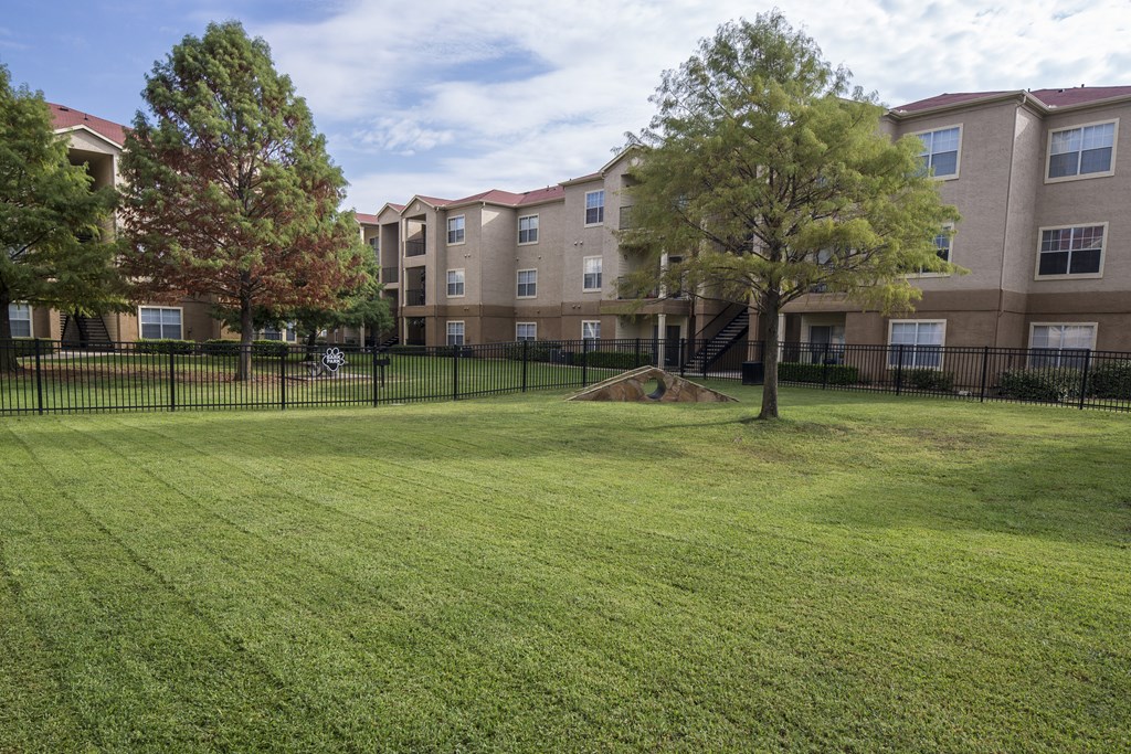 a grassy area with trees in front of an apartment building