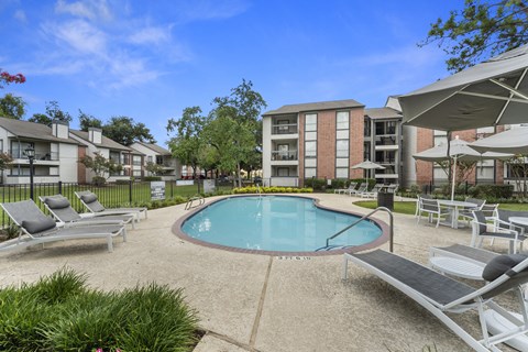 A swimming pool surrounded by lounge chairs and umbrellas in a residential area.