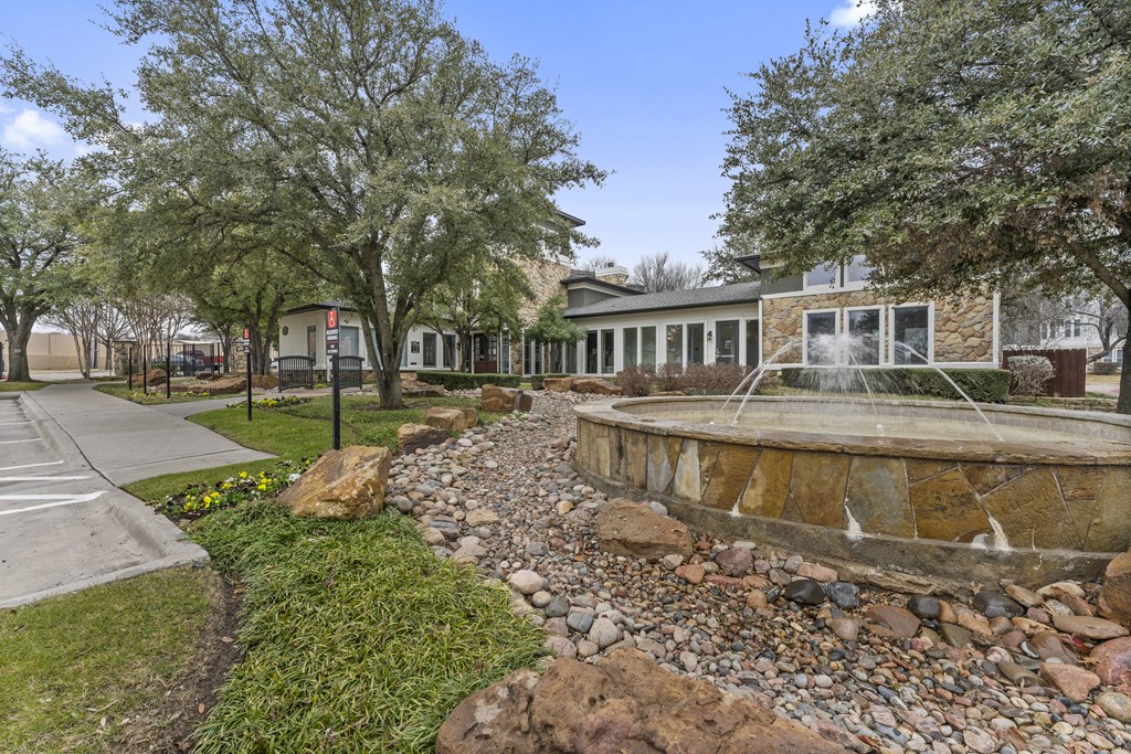 a fountain in front of a building with trees and rocks