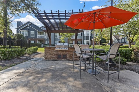 a patio with an umbrella and tables with chairs and a grill