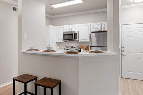 A kitchen with white cabinets and a counter with two stools.