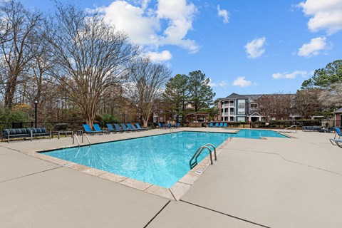 A large swimming pool surrounded by trees and chairs.