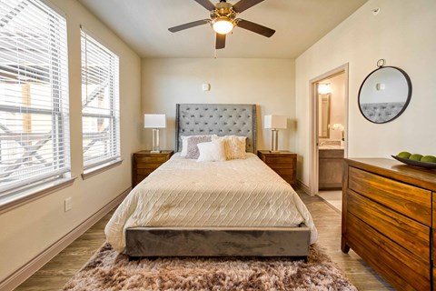 A bedroom with a large bed, a ceiling fan, and a rug on the floor.