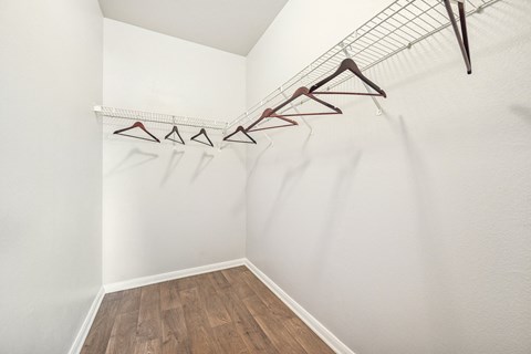 a room with white walls and wood flooring and a closet with clothes hangers
