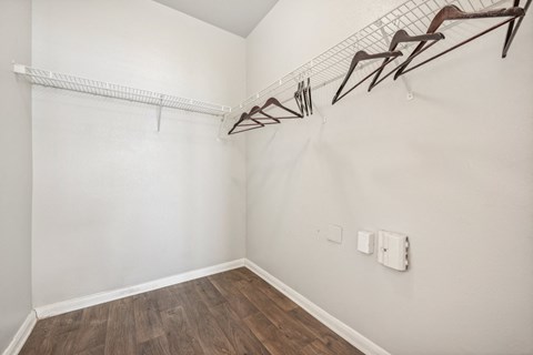 an empty room with white walls and wood flooring and a white closet with hooks