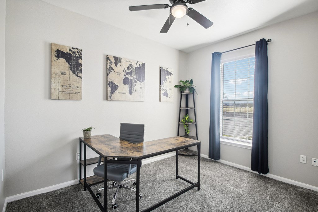 an office with a desk and a ceiling fan and a window