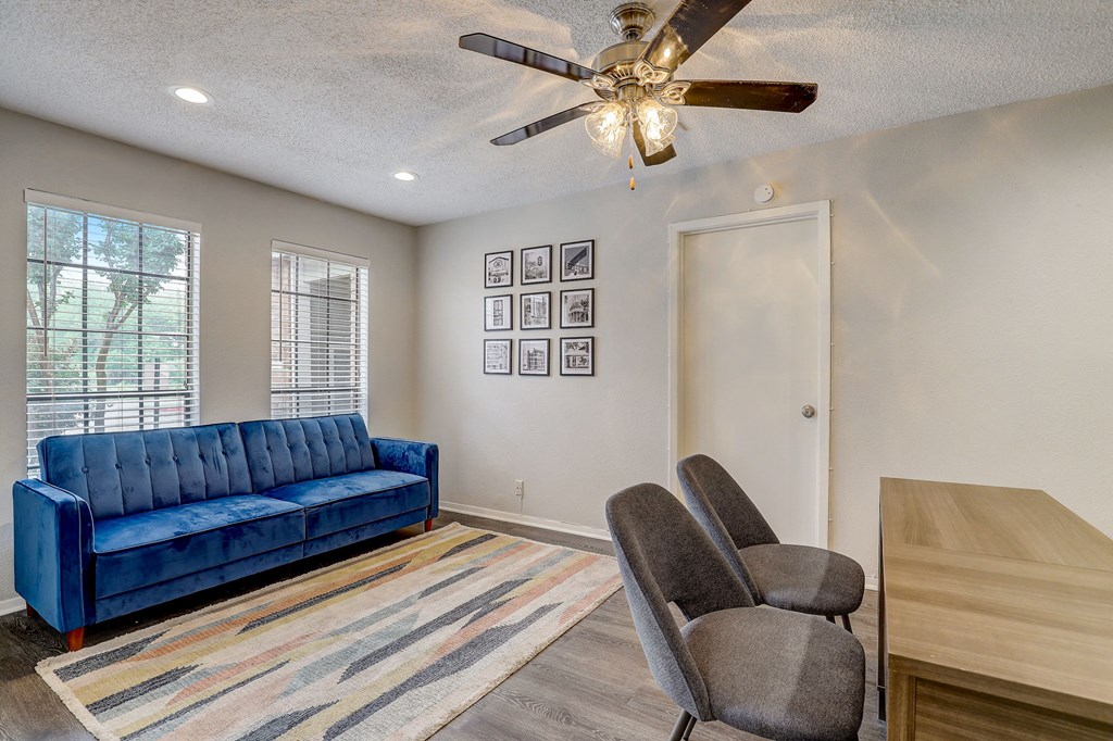 a living room with a blue couch and chairs and a ceiling fan