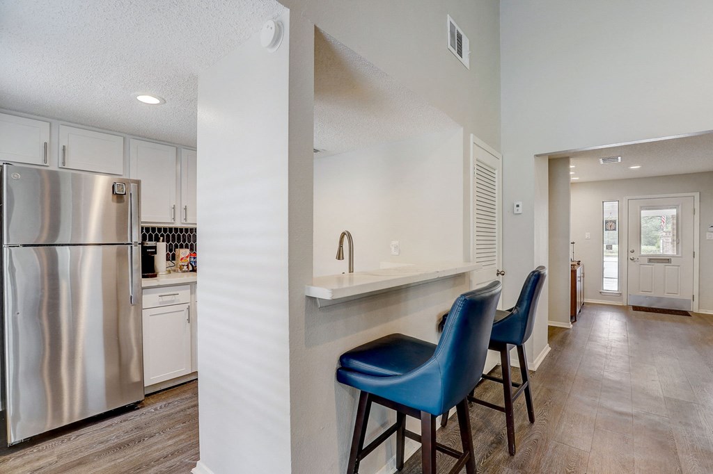 a kitchen with a bar with blue chairs and a stainless steel refrigerator