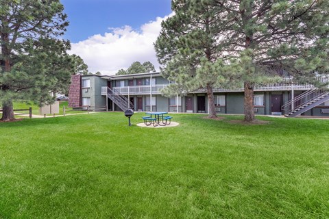 A grassy area in front of a building with a bench and trees.