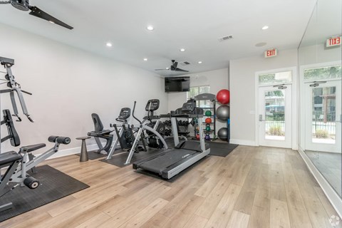 A well-equipped gym with a variety of exercise machines and a ceiling fan.