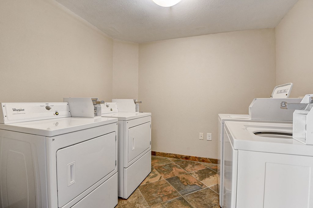 an empty laundry room with four white washers and dryers and two sets of