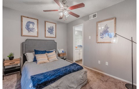 A bedroom with a bed, a ceiling fan, and three wall art pieces.