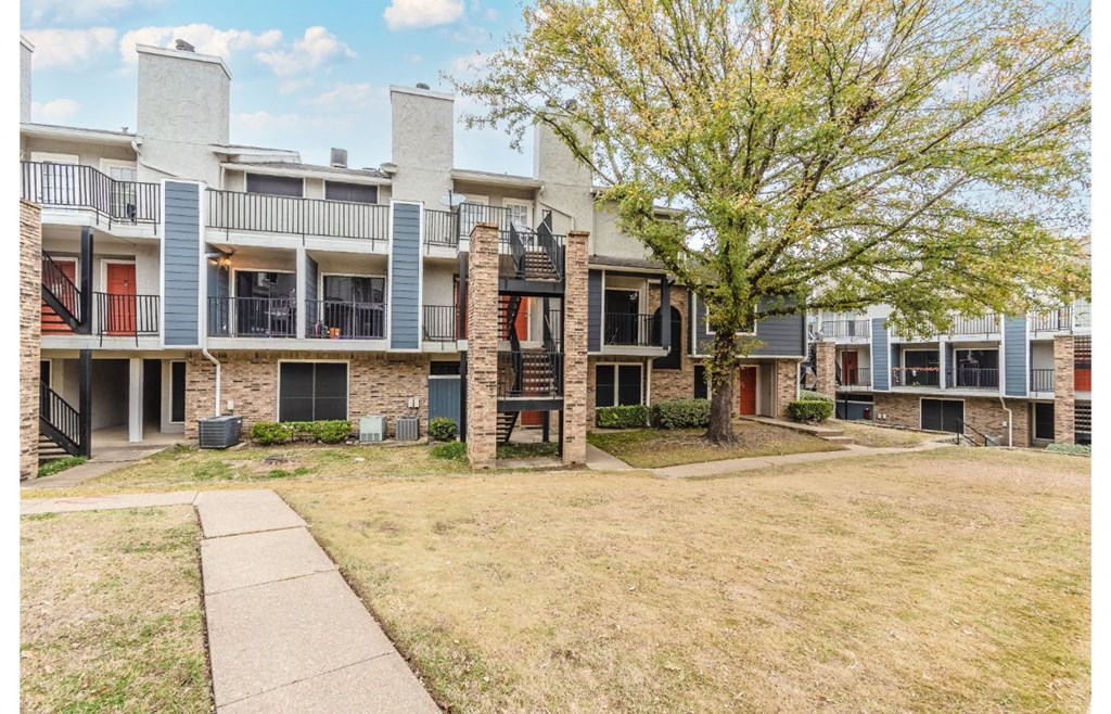 an exterior view of an apartment building with grass and a tree