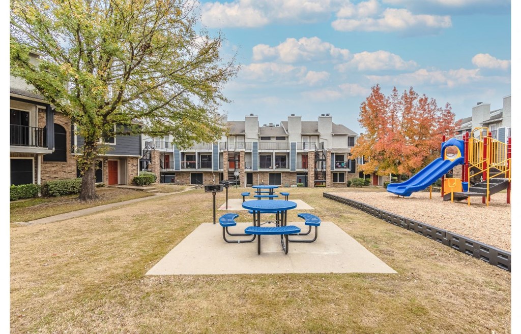 a playground and picnic table in a park with apartments in the background