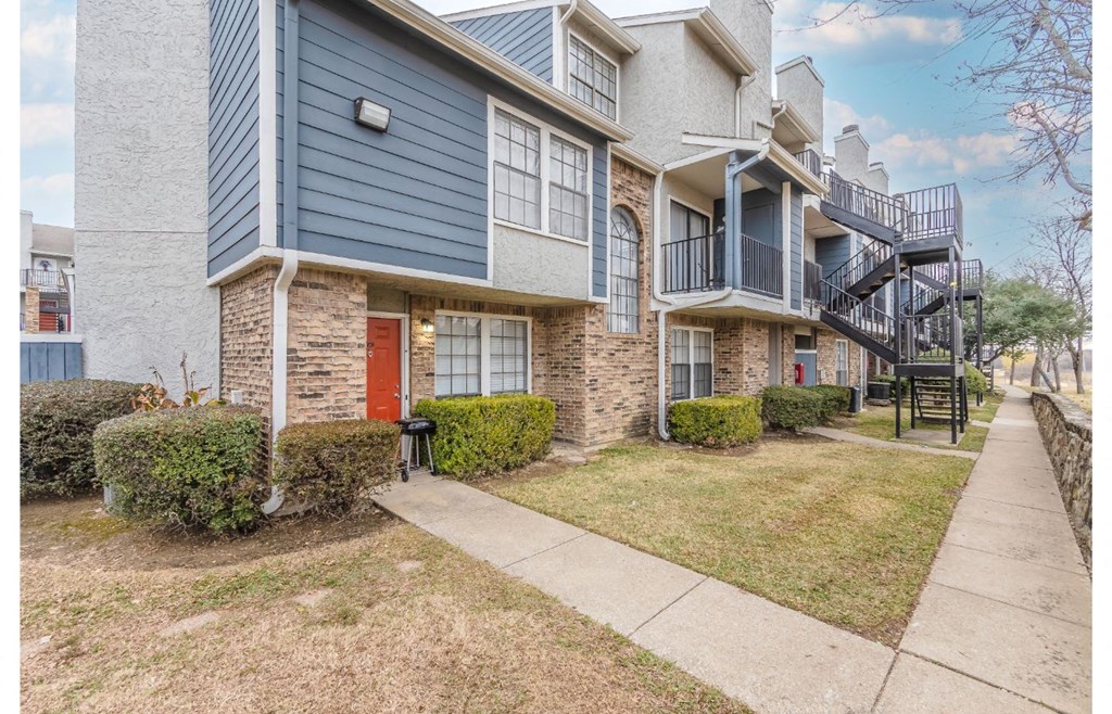 a sidewalk in front of an apartment building with a red door