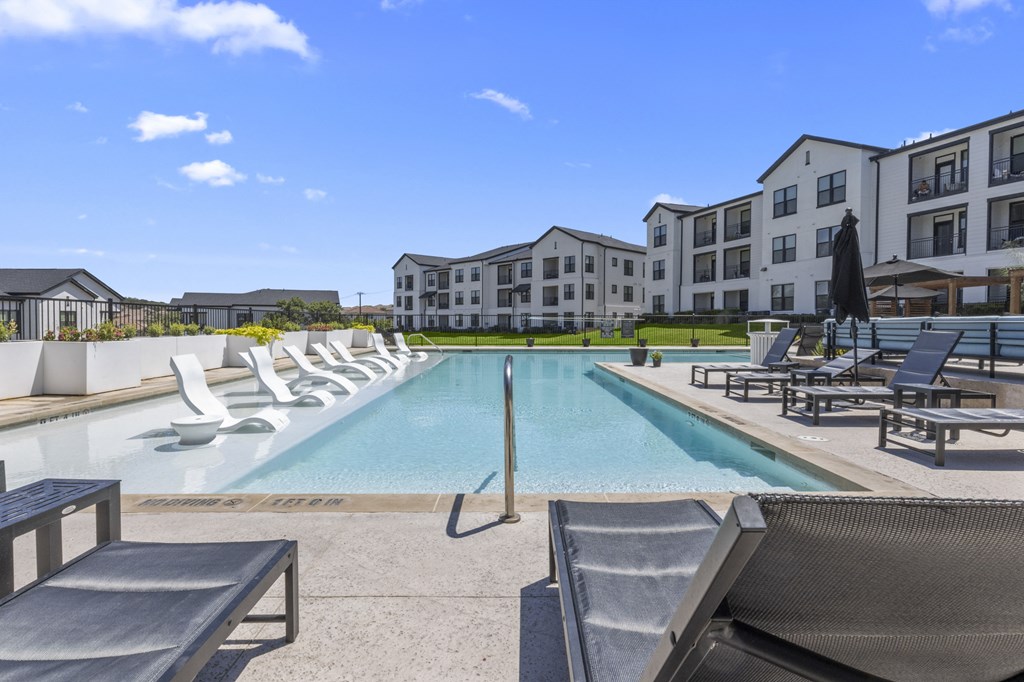 a swimming pool with lounge chairs and buildings in the background