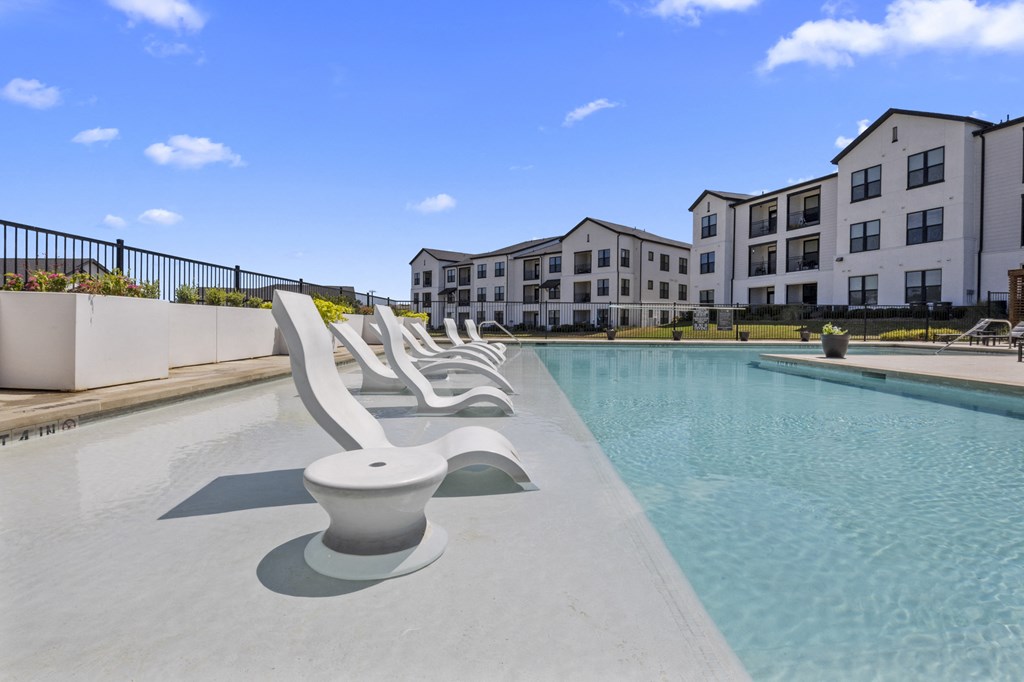a pool with a row of chairs in front of an apartment building