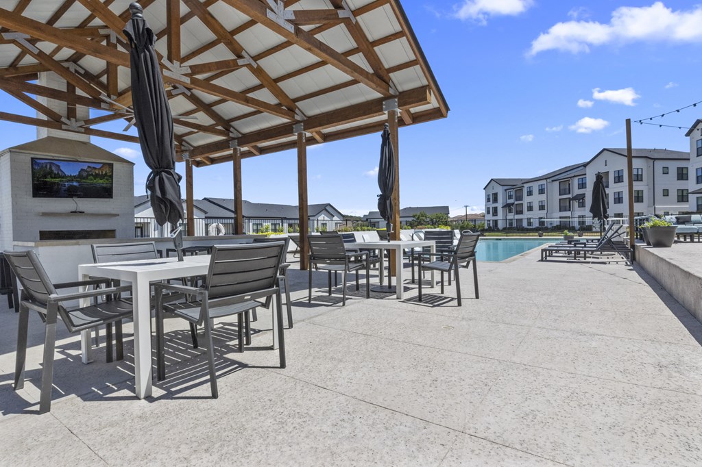 a covered patio with tables and chairs next to a swimming pool