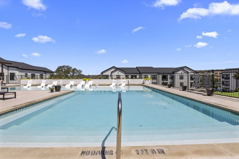 a swimming pool with white chairs around it and apartments in the background