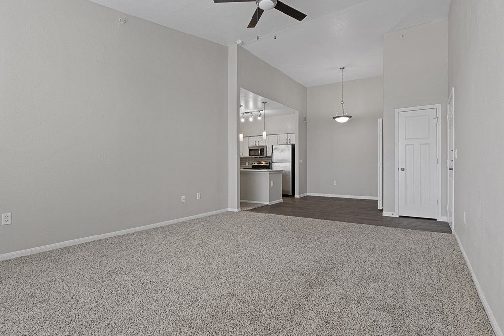 an empty living room with a ceiling fan and a kitchen