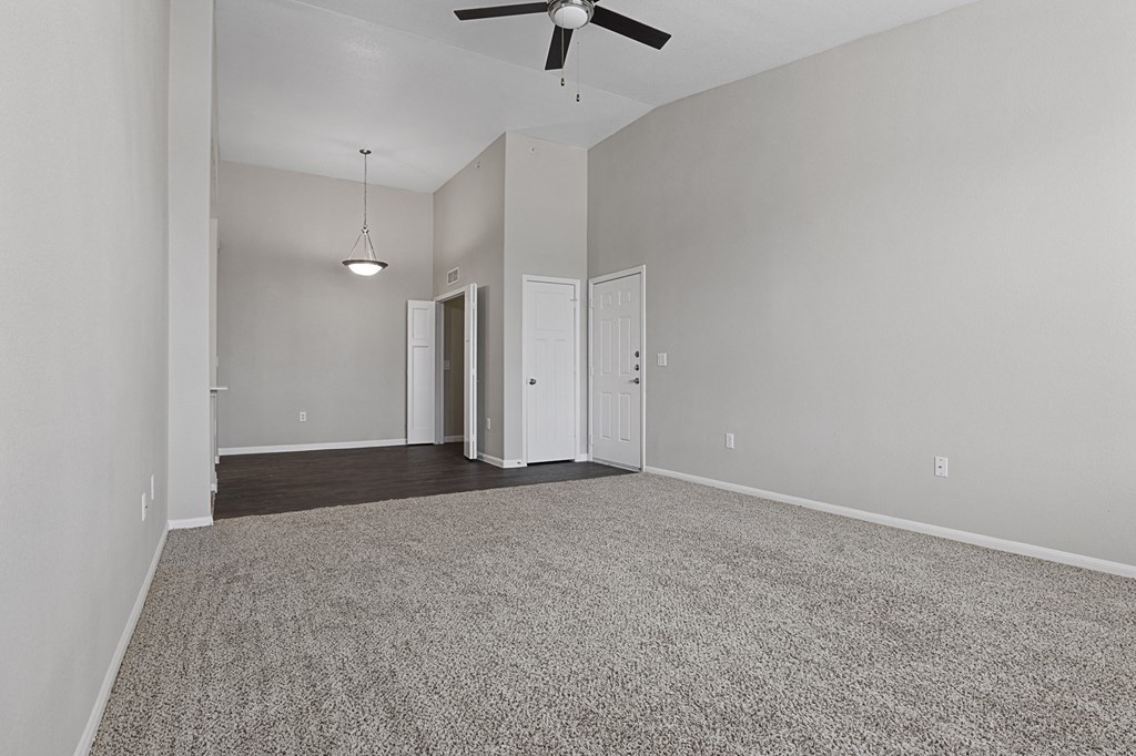 an empty living room with a ceiling fan and a carpet