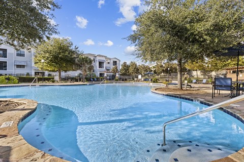 A swimming pool surrounded by trees and a building in the background.