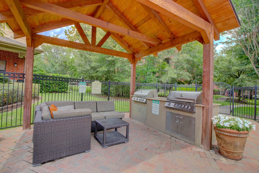 an outdoor kitchen with a grill and a seating area under a wooden awning