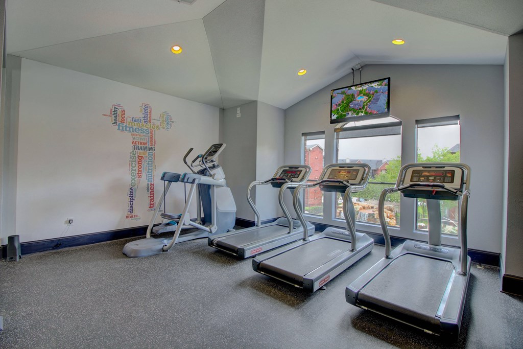 a workout room with treadmills and a tv