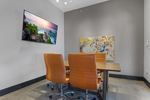 Two orange chairs are placed in front of a table with a painting and a picture on the wall.