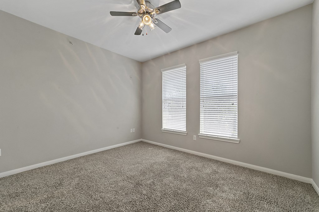 an empty room with a ceiling fan and two windows