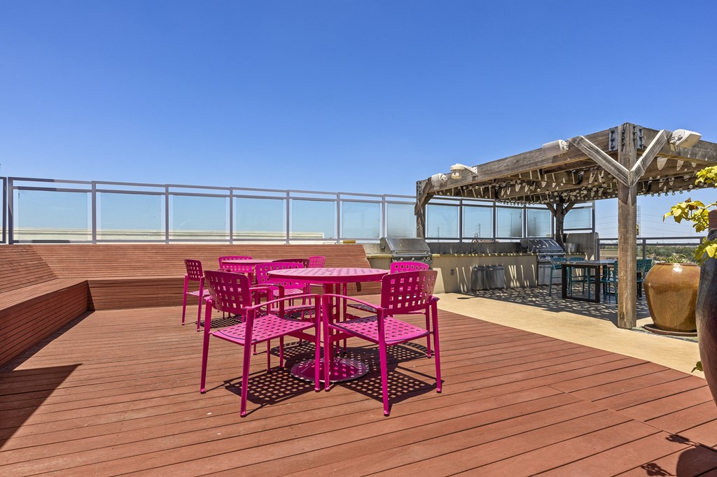 a patio with pink chairs and a table on a deck overlooking the ocean