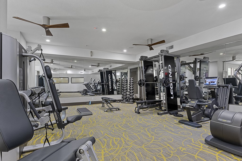 a gym with cardio equipment and weights in a building with white walls and yellow carpet