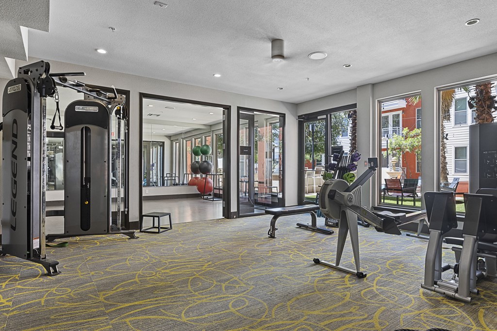 a gym with cardio machines and weights in a room with windows