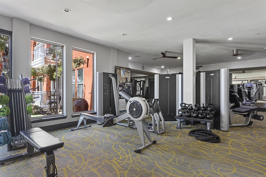 a gym with weights and cardio equipment in a room with windows