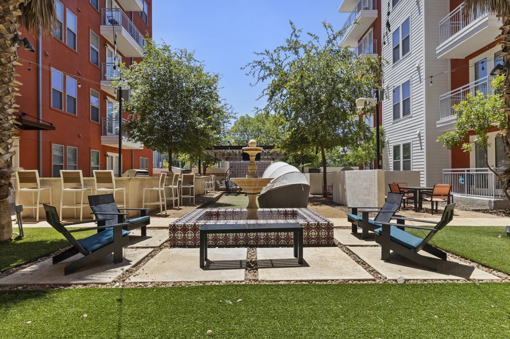 a fountain sits in the middle of a courtyard with benches and chairs