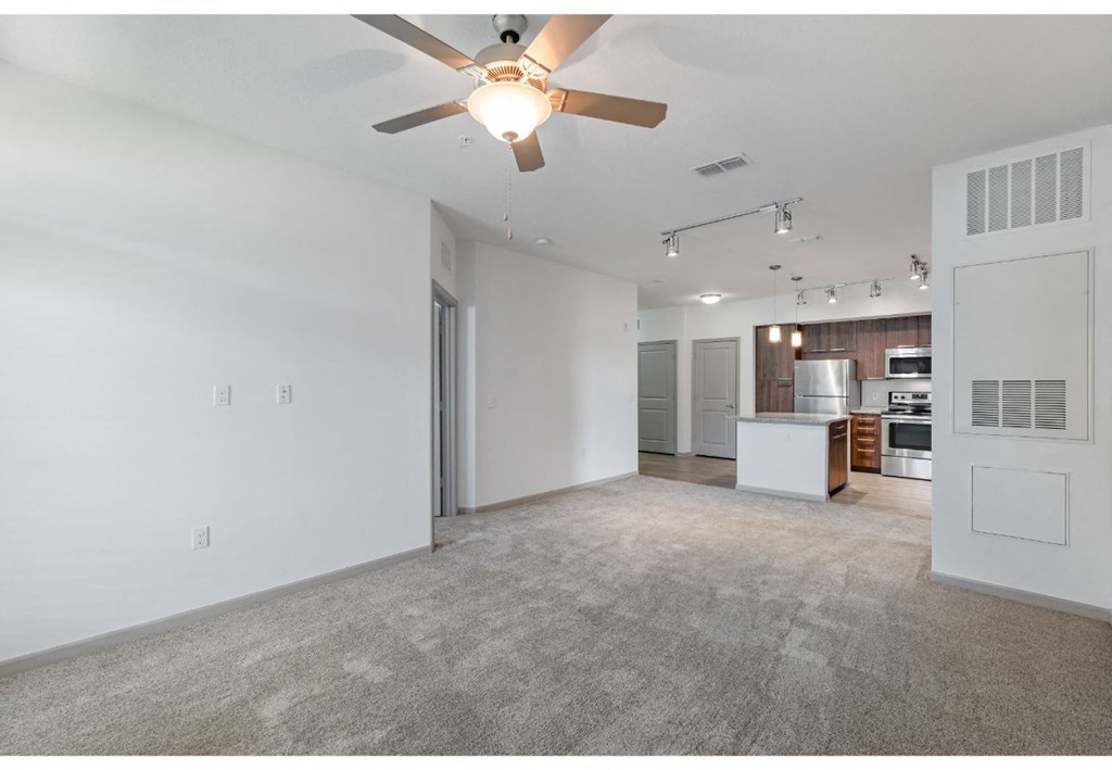 an empty living room with a ceiling fan and a kitchen