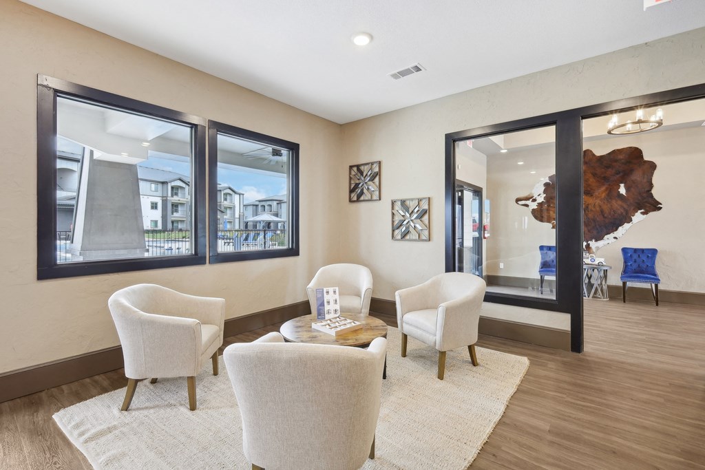a living room with white chairs and a rug and large windows