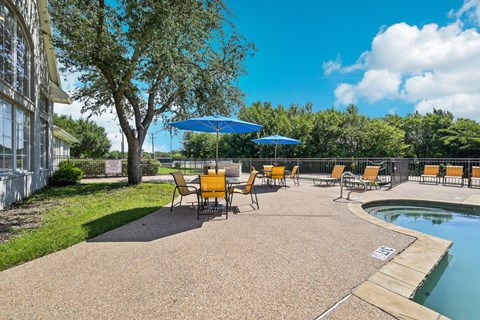 a patio with chairs and umbrellas next to a pool
