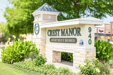 Crest Manor Apartment Homes sign with a stone pillar and a green lawn.