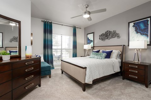 Apartment bedroom with large window, ceiling fan, dresser, and nightstands.