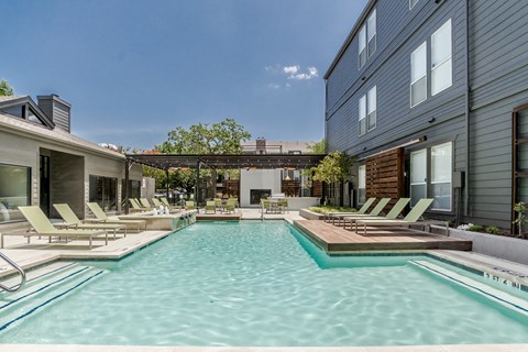 a pool with lounge chairs and a hot tub in front of a building
