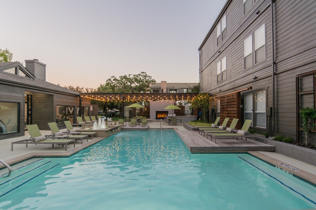 a pool with lounge chairs and umbrellas at dusk