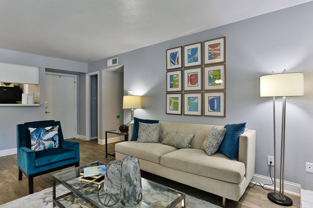 A living room with a blue chair, a beige couch, and a glass coffee table.