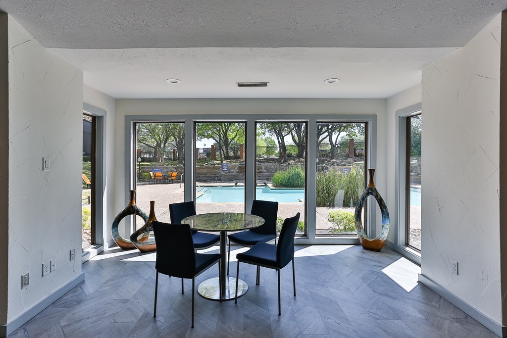 A dining room with a table and chairs and a view of a pool and trees outside.