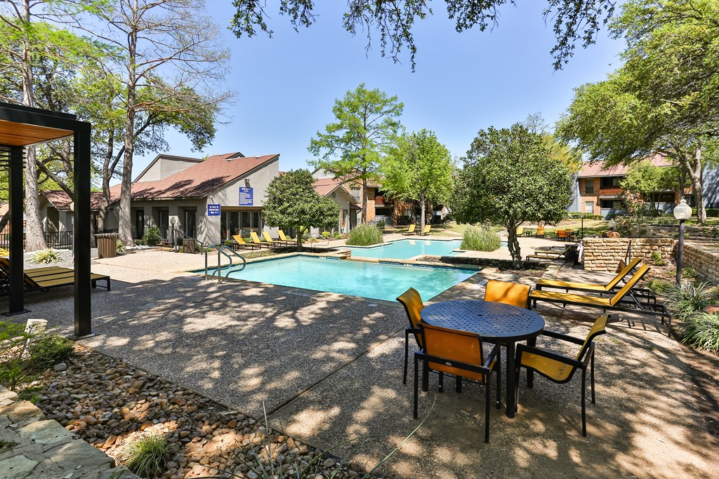 A pool surrounded by chairs and trees.