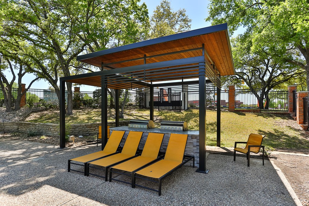 A park bench with a yellow and black design is situated under a wooden and metal shelter.