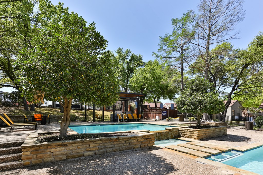 A pool surrounded by trees and a stone wall.